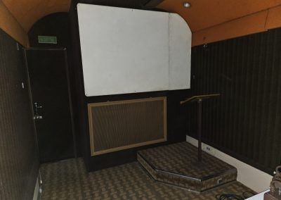 L'écran de la voiture SCC 66 était configurable en version 4:3 ou panoramique avec des panneaux amovibles (ici il manque la panneau de gauche). Le pupitre fixe monté sur une petite estrade pour un usage en mode conférence (au mur les prises micro). Photo Arnaud Guyon 22-11-2025.